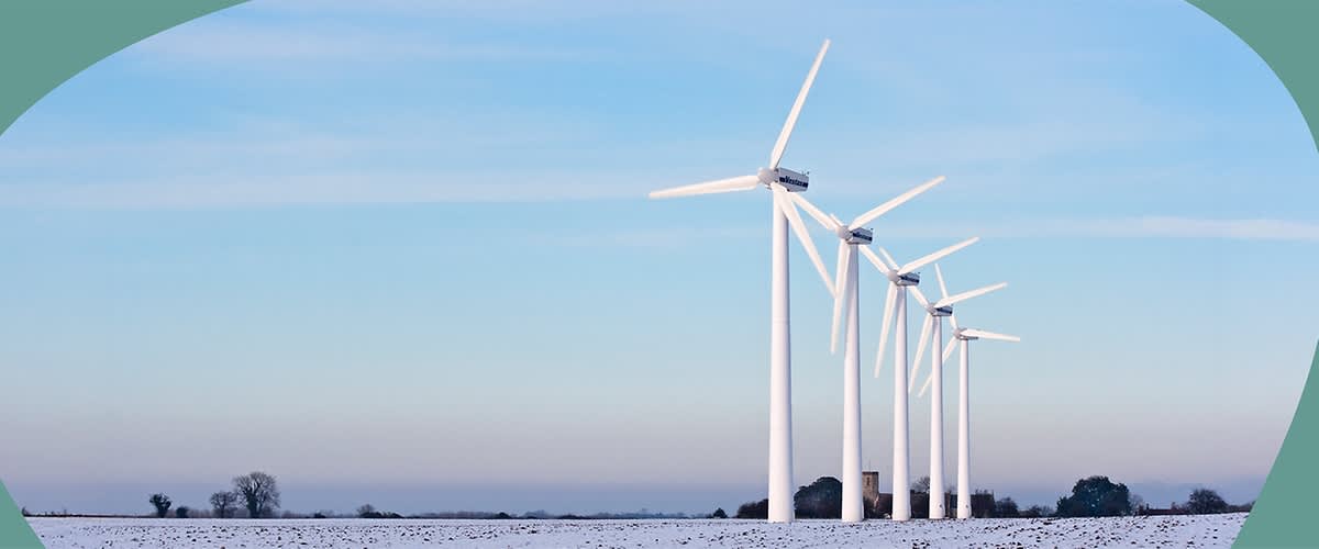 Fünf weiße Windräder stehen in einer verschneiten Landschaft unter blauem Himmel