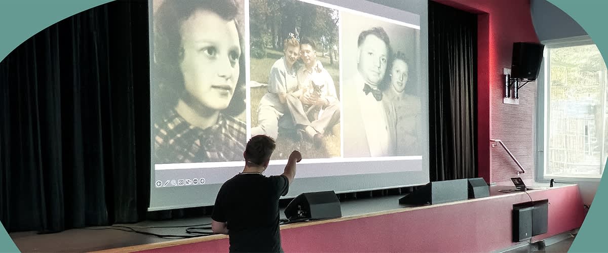 Luke Schaaf steht vor einer Leinwand, auf der drei historische Fotos von Ruth Wertheim projiziert werden.