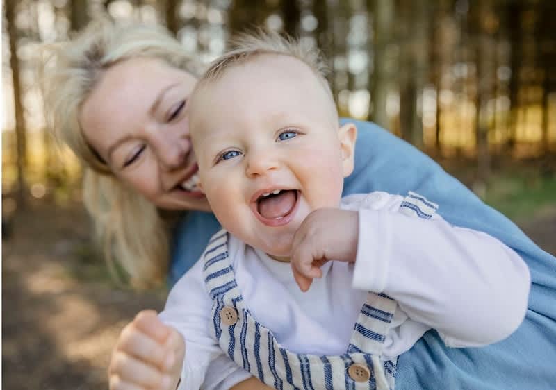 Eine Frau hält ein lachendes Baby im Arm. Zu sehen sind die ersten Milchzähne