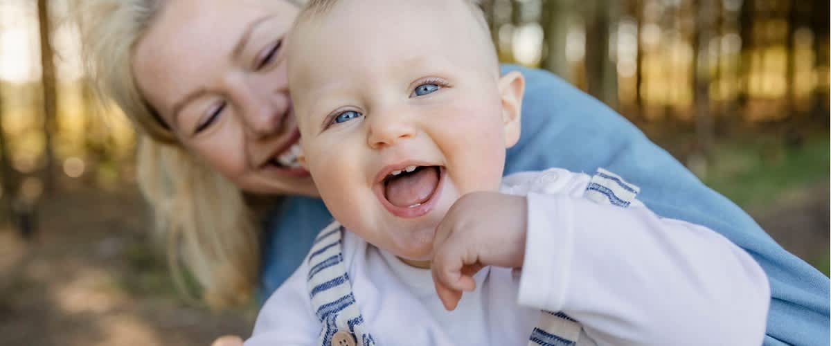 Eine Frau hält ein lachendes Baby im Arm. Zu sehen sind die ersten Milchzähne