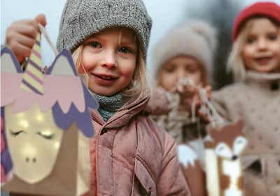 Zwei Kinder in Winterkleidung halten selbstgebastelte Laternen mit Sternenmuster in der Hand