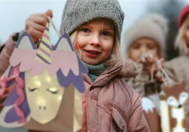 Zwei Kinder halten selbstgebastelte Laternen, eine in Form eines Einhorns mit leuchtenden Augen und bunter Mähne, die andere in Form eines Fuchses mit Ohren und Schnauze