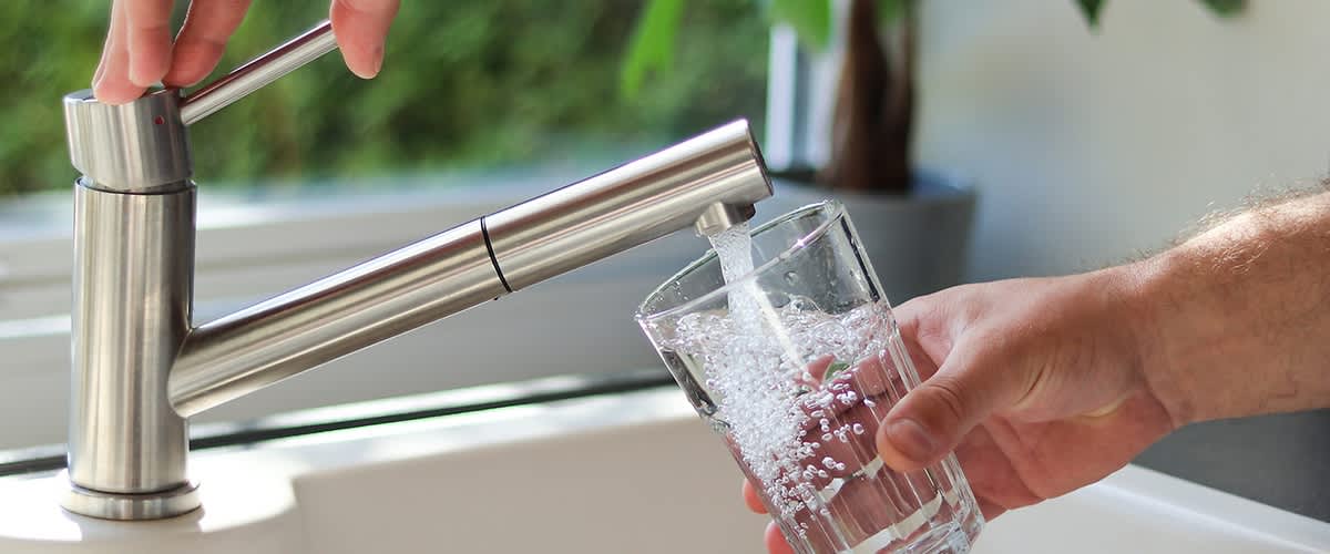 Hand hält ein fast volles Glas unter einen offenen Wasserhahn.