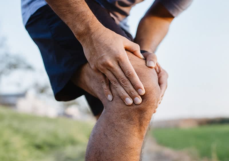 Männliches Bein in blauer Sporthose. Der Mann hält sich nach einem Krampf das Knie.