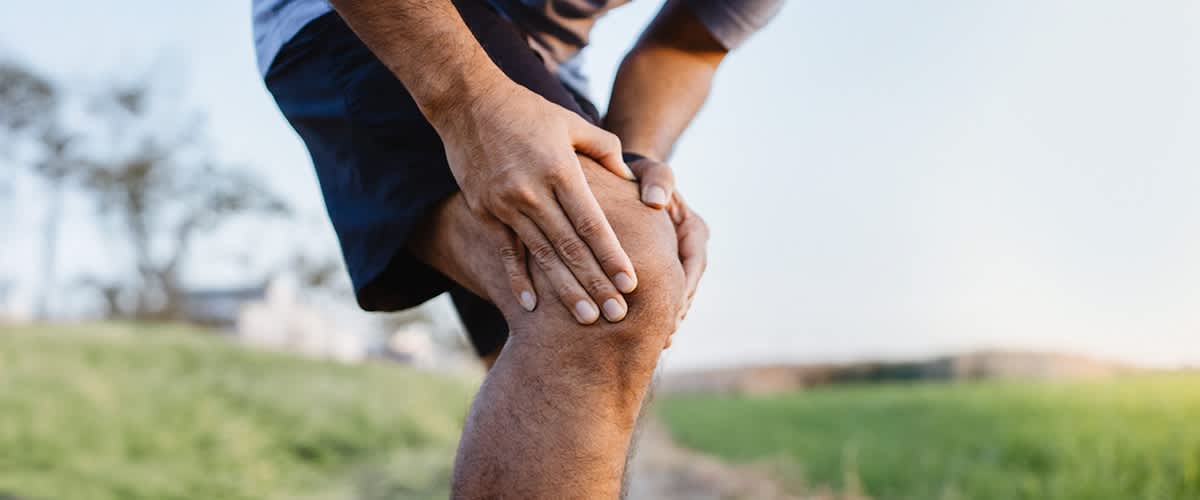 Männliches Bein in blauer Sporthose. Der Mann hält sich nach einem Krampf das Knie.