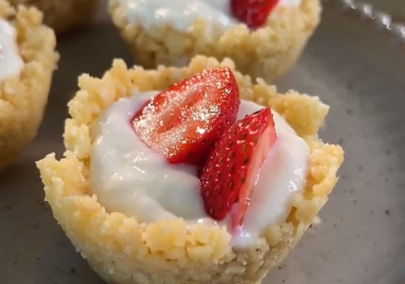 Ein Dessert aus einem krümeligen Teigboden, gefüllt mit weißer Creme und garniert mit frischen Erdbeerscheiben