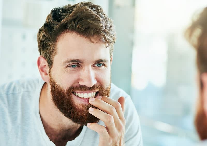 Ein Mann in einem weißen T-Shirt berührt sein Zahn mit der Hand