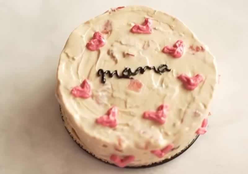 Ein runder Kuchen mit weißer Glasur, verziert mit rosa Herzchen und dem Schriftzug „mama“ in schwarzer Schrift