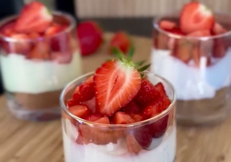 Drei Gläser mit Schichten aus Joghurt und frischen Erdbeeren, das vordere Glas ist im Fokus