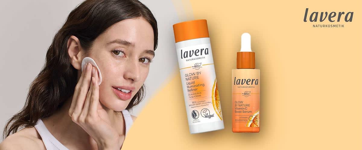 Zwei Lavera-Naturkosmetikprodukte auf beigem Hintergrund: links weiße Flasche mit orangefarbener Kappe und Schrift „Glow by Nature Liquid Illuminating Refiner“, rechts orangefarbene Glasflasche mit Pipette und Schrift „Glow by Nature Vitamin C Boost Serum“, oben rechts Lavera-Logo
