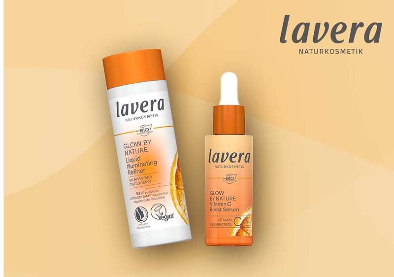 Zwei Lavera-Naturkosmetikprodukte vor hellorange Hintergrund: links eine weiße Flasche mit orangefarbenem Deckel und Aufschrift „Glow by Nature Liquid Illuminating Refiner“, rechts ein orangefarbenes Pipettenfläschchen mit Aufschrift „Glow by Nature Vitamin C Boost Serum“ und dem Lavera-Logo oben