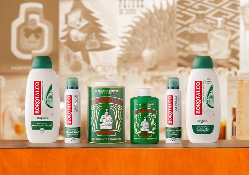 Sechs Borotalco-Produkte auf einem Tisch, darunter zwei weiße Duschgel-Flaschen mit rotem Borotalco-Logo, eine grüne Dose mit weißem Logo, ein grüner Behälter mit rotem Logo, ein weißer Deo-Stick und ein weißes Deo-Spray mit rotem Logo