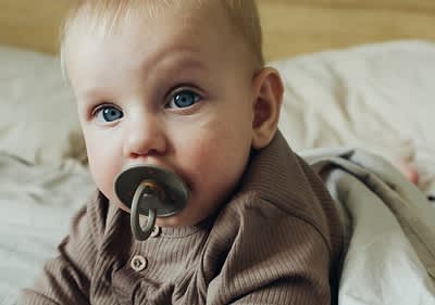 Baby mit olivgrünem Schnuller im Mund