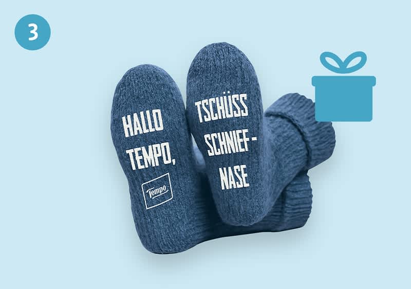 Zwei blaue Socken mit den weißen Aufschriften „HALLO TEMPO!“ und „TSCHÜSS SCHNIEFNASE“ sowie einem kleinen Tempo-Logo, daneben ein Geschenk-Symbol