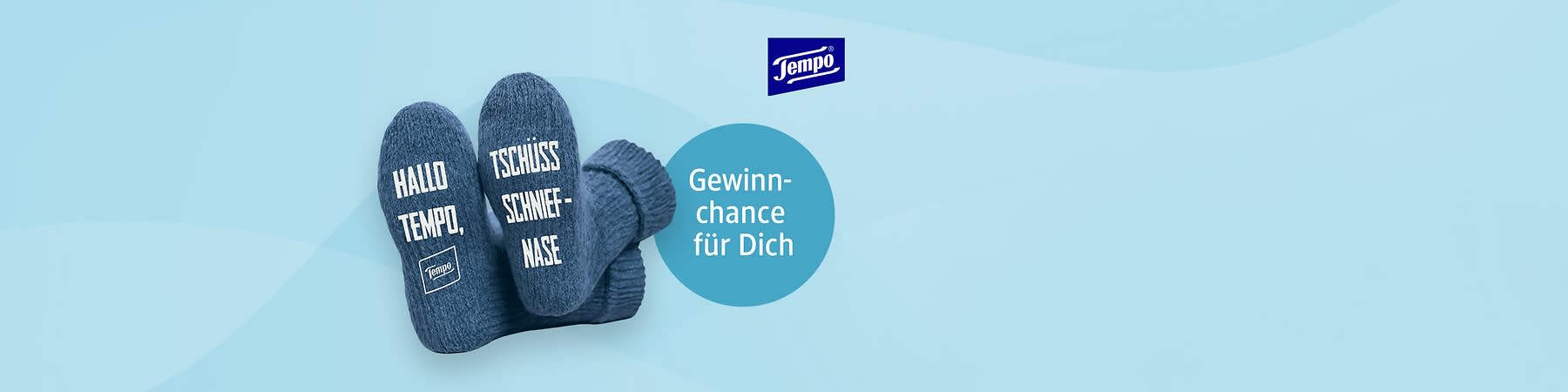 Zwei blaue Socken mit den Aufschriften „Hallo Tempo,“ und „Tschüss Schniefnase“ liegen nebeneinander, daneben ein blauer Kreis mit dem Text „Gewinnchance für Dich“ und das Tempo-Logo oben rechts