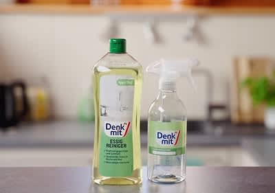 Zwei Flaschen der Marke Denk mit, links eine große Flasche Essigreiniger mit grünem Verschluss und der Aufschrift „Essig Reiniger“, rechts eine kleinere Sprühflasche mit der Aufschrift „Denk mit“