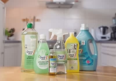 Sechs Reinigungsprodukte der Marke Denkmit stehen auf einem Tisch, darunter Essigreiniger, Spülsam, Allzweckreiniger, Glasreiniger, Waschmittel und ein weiteres Reinigungsmittel