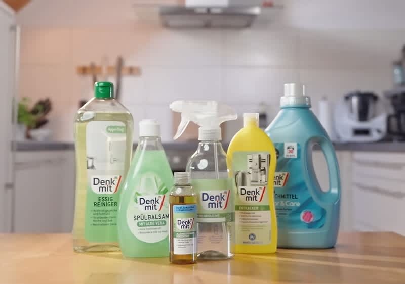 Sechs Reinigungsprodukte der Marke Denkmit stehen auf einem Tisch, darunter Essigreiniger, Spülsam, Allzweckreiniger, Glasreiniger, Waschmittel und ein weiteres Reinigungsmittel