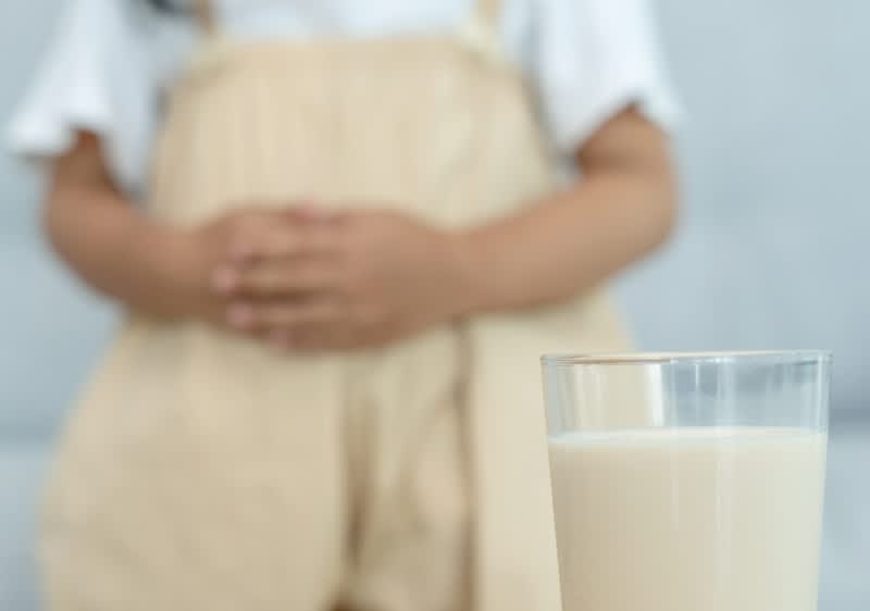 Im Hintergrund hält sich jemand den Bauch. Im Vordergrund steht ein Glas Milch.