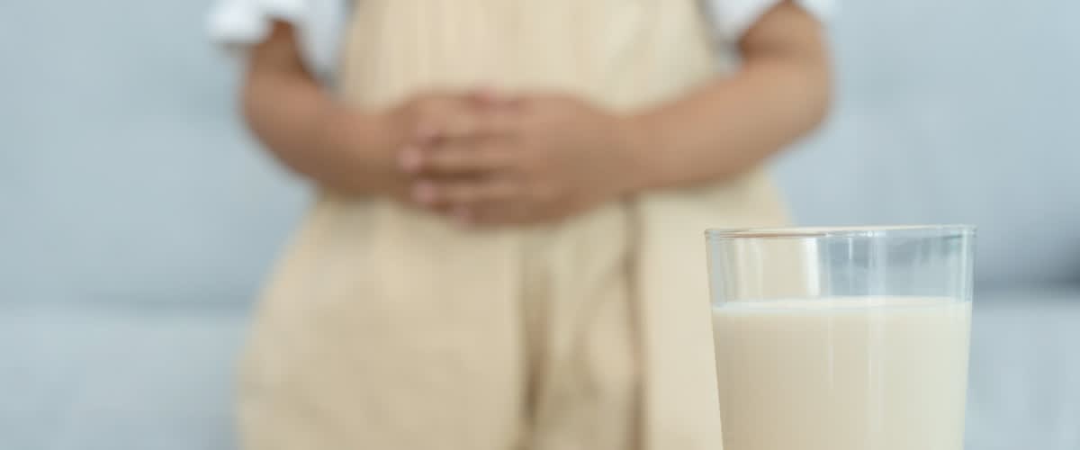Im Hintergrund hält sich jemand den Bauch. Im Vordergrund steht ein Glas Milch.