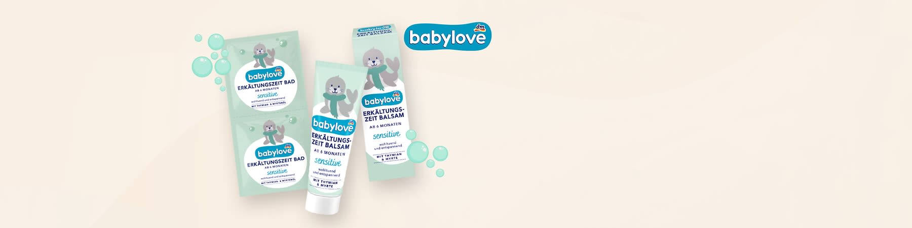 Produktverpackungen der Marke babylove mit einem niedlichen Robben-Design, bestehend aus zwei grünen Sachets mit der Aufschrift „Erkältungszeit Bad ab 6 Monaten sensitive“ und einer grünen Tube mit der Aufschrift „Erkältungszeit Balsam ab 6 Monaten sensitive“