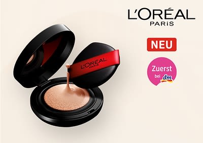 Eine schwarze Puderdose mit offenem Deckel zeigt eine beige Foundation, daneben ein schwarzer Applikator mit rotem Band und der Aufschrift „L'Oréal Paris“, darüber steht „NEU“ in einem roten Kasten, daneben „Zuerst bei dm“ in einem rosa Kreis, oben rechts das Logo von L'Oréal Paris