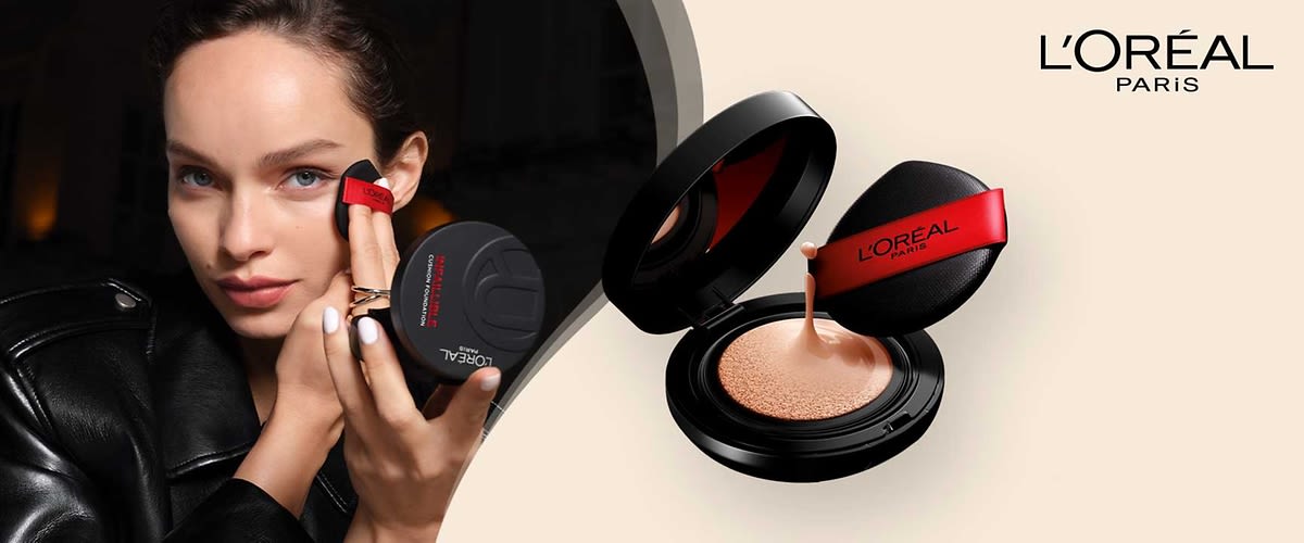 Eine schwarze Puderdose mit offenem Deckel zeigt eine beige Foundation, daneben ein schwarzer Applikator mit rotem Band und der Aufschrift „L'Oréal Paris“, oben rechts das Logo von L'Oréal Paris