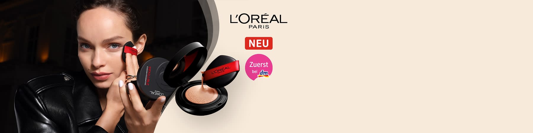 Eine geöffnete schwarze Puderdose mit einem roten Applikator und flüssigem Make-up, daneben die Aufschrift „L'Oréal Paris“, „NEU“ und „Zuerst bei dm“