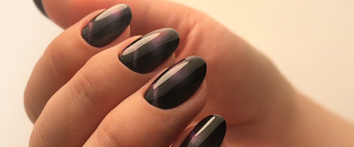 Nahaufnahme einer Hand mit ovalen, dunkel lackierten Fingernägeln, die einen schimmernden violetten Akzent haben