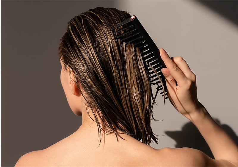 Eine Person kämmt ihr nasses, schulterlanges Haar mit einem schwarzen Kamm