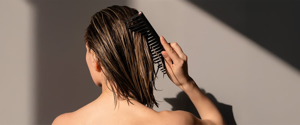 Eine Person kämmt ihr nasses, schulterlanges Haar mit einem schwarzen Kamm