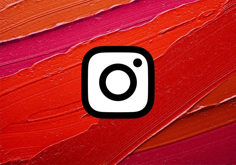 Das Logo von Instagram vor einem Hintergrund aus roten und orangefarbenen Pinselstrichen