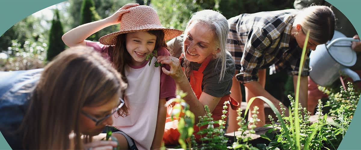 Mehrere Personen arbeiten in einem Garten, einige beugen sich über Pflanzen, während eine Person eine Gießkanne hält.