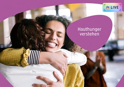 Zwei Personen umarmen sich herzlich, eine trägt ein gestreiftes Hemd, die andere eine gelbe Jacke. Rechts im Bild steht der Text „Hauthunger verstehen“ in einem lila Bereich. Oben rechts ist ein kleines Logo mit der Aufschrift „dmLIVE“