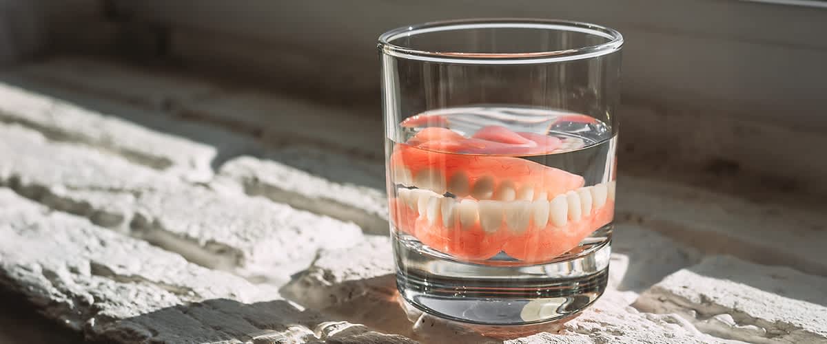 In einem Glas Wasser liegt im Sonnenschein eine Zahnprothese