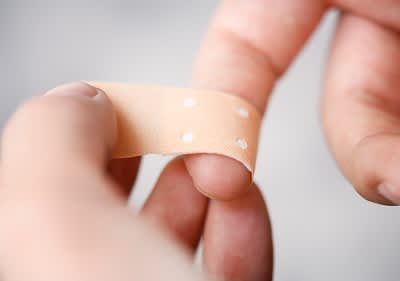 Auf einen Finger wird eine Schnittwunde mit einem Pflaster überklebt.