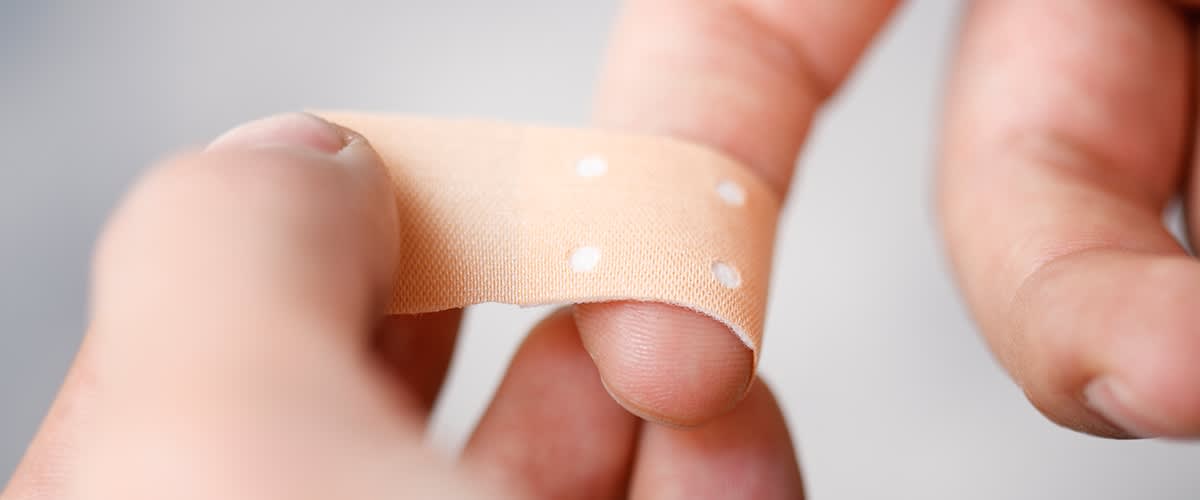 Auf einen Finger wird eine Schnittwunde mit einem Pflaster überklebt.