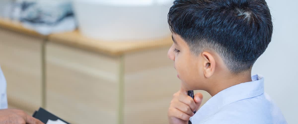 Ein Mann hält ein Buch mit einer bunten Illustration eines Gehirns in der Hand, während er mit einem Jungen spricht, dessen Gesicht unscharf ist