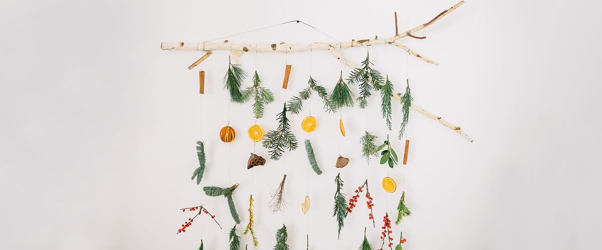 Ein Ast mit daran hängenden natürlichen Dekorationen wie getrocknete Orangenscheiben, Zimtstangen, Tannenzweigen und roten Beeren