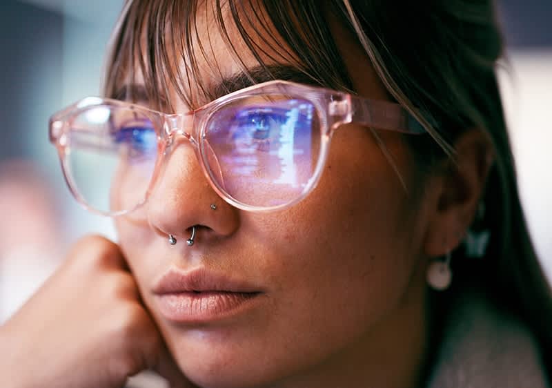 Eine Person trägt eine Brille mit einem rosafarbenen Rahmen und eine Perlenohrring