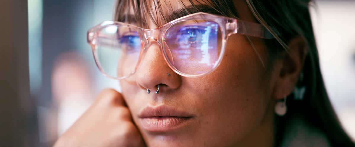 Eine Person trägt eine Brille mit einem rosafarbenen Rahmen und eine Perlenohrring