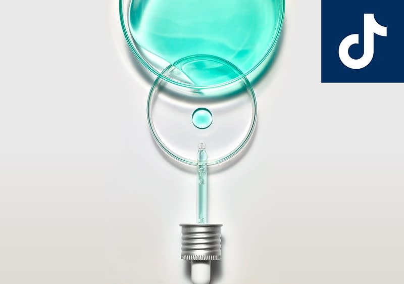 Eine Pipette mit silbernem Verschluss tropft eine klare, türkisfarbene Flüssigkeit auf eine kreisförmige Glasoberfläche, oben rechts das Logo von TikTok