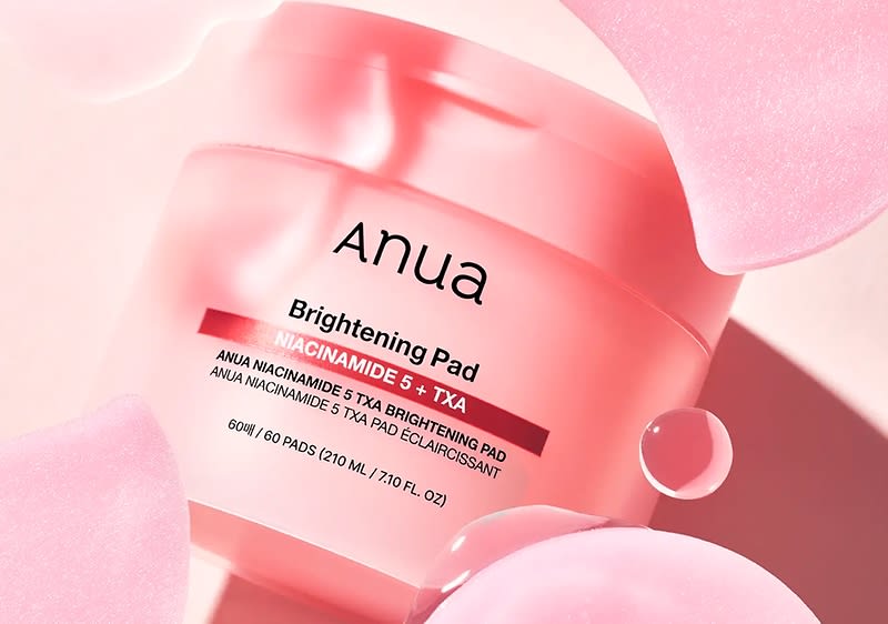 Eine rosafarbene Verpackung der Anua Brightening Pads mit der Aufschrift „Niacinamide 5% + TXA“ und „60 Pads (210 ml / 7.10 fl. oz.)“