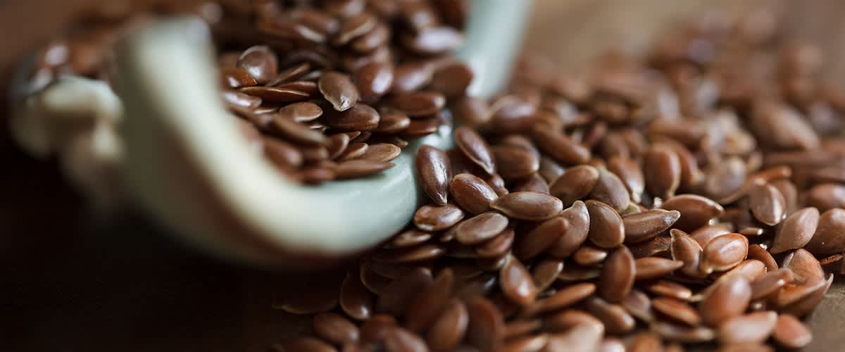 Schwarzkümmel liegt auf einem Holzlöffel und ist teilweise auf einer grauen Oberfläche verstreut