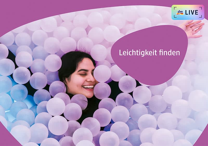 Eine Person liegt in einem Bällebad aus weißen und lilafarbenen Bällen, der Text „Leichtigkeit finden“ ist in weißer Schrift auf einem lilafarbenen Hintergrund zu sehen, oben rechts befindet sich das dmLIVE Logo