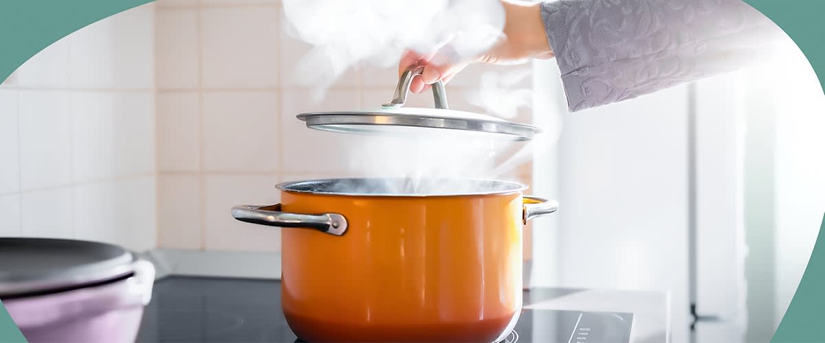 Ein orangefarbener Topf auf einem Herd, aus dem Dampf aufsteigt, während eine Hand den Deckel anhebt
