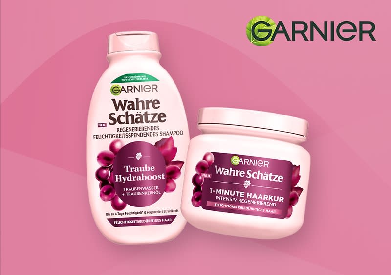 Zwei Produktverpackungen von Garnier Wahre Schätze auf rosa Hintergrund, links eine hell-rosa Flasche mit der Aufschrift „Wahre Schätze Traube Hydraboost Regenerierendes Feuchtigkeitsspendendes Shampoo“, rechts ein hell-rosa Tiegel mit der Aufschrift „Wahre Schätze 1-Minute Haarkur Intensiv Regenerierend“. Auf der linken Seite des Bildes eine lächelnde Frau mit gesundem, braunem Haar