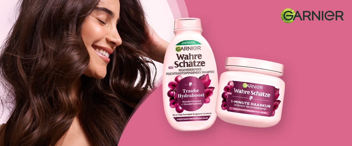 Zwei Produktverpackungen von Garnier Wahre Schätze auf rosa Hintergrund, links eine hell-rosa Flasche mit der Aufschrift „Wahre Schätze Traube Hydraboost Regenerierendes Feuchtigkeitsspendendes Shampoo“, rechts ein hell-rosa Tiegel mit der Aufschrift „Wahre Schätze 1-Minute Haarkur Intensiv Regenerierend“. Auf der linken Seite des Bildes eine lächelnde Frau mit gesundem, braunem Haar