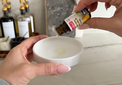 Eine Person tropft ätherisches Öl aus einer kleinen Flasche in eine weiße Keramikschale