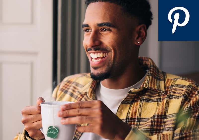 Ein Mann in kariertem Hemd hält eine Tasse mit einem Teebeutel der Marke Pukka, oben rechts das Logo von Pinterest